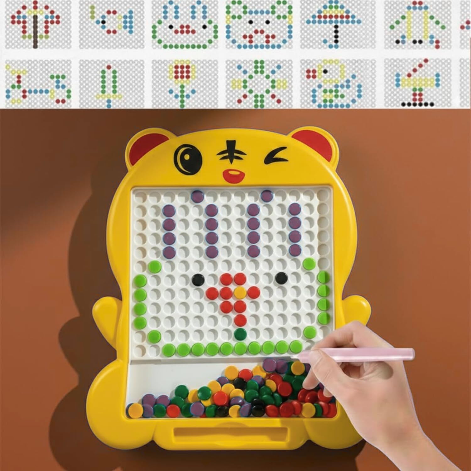 A yellow cartoon cat-shaped pegboard drawing toy with a hand holding a pink stylus, shown on a brown background. The top of the image shows a row of example dot patterns that can be assembled on the board.